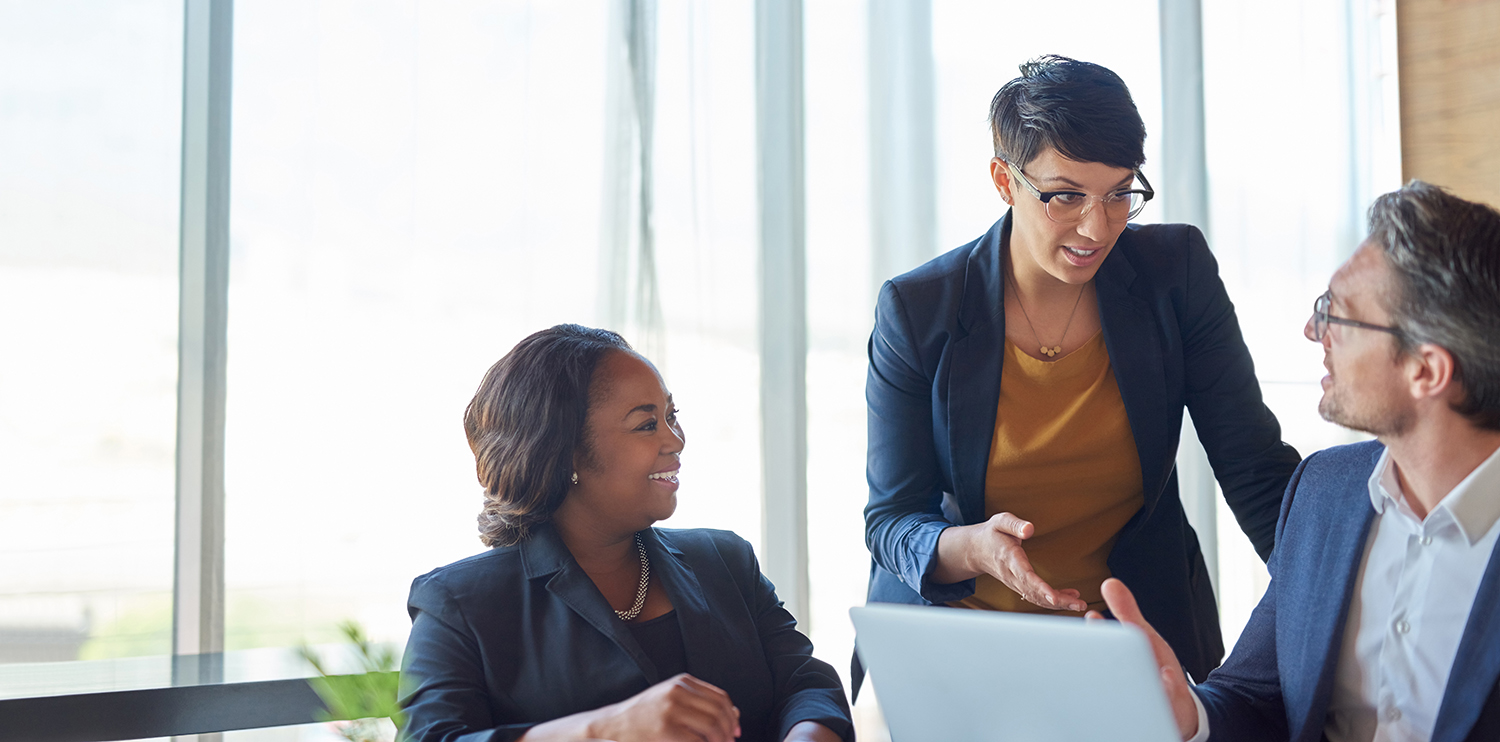 two female and one male colleague speak at a desk